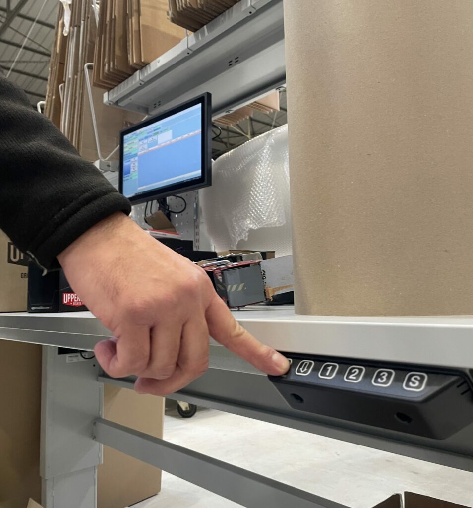 Une main appuie sur un bouton d'une table de préparation ajustable.